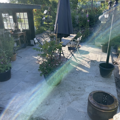 Færdig fliseterrasse i Ellinge med møbler og planter i haven.