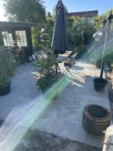 Færdig fliseterrasse i Ellinge med møbler og planter i haven.